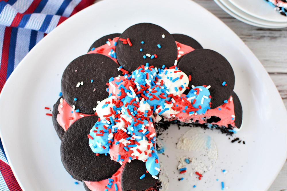 A red, white, and blue icebox cake with chocolate wafers, with a slice cut out of it