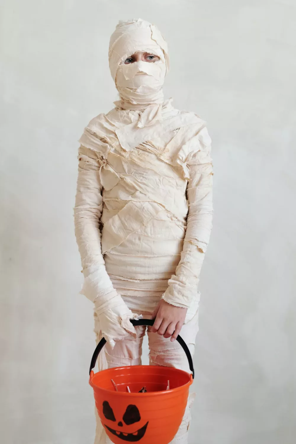 person dressed as a mummy holding a trick or treat pail