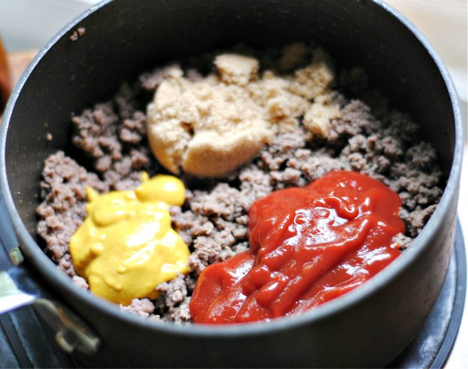 ground beef in a pot with brown sugar, yellow mustard and red ketchup on top