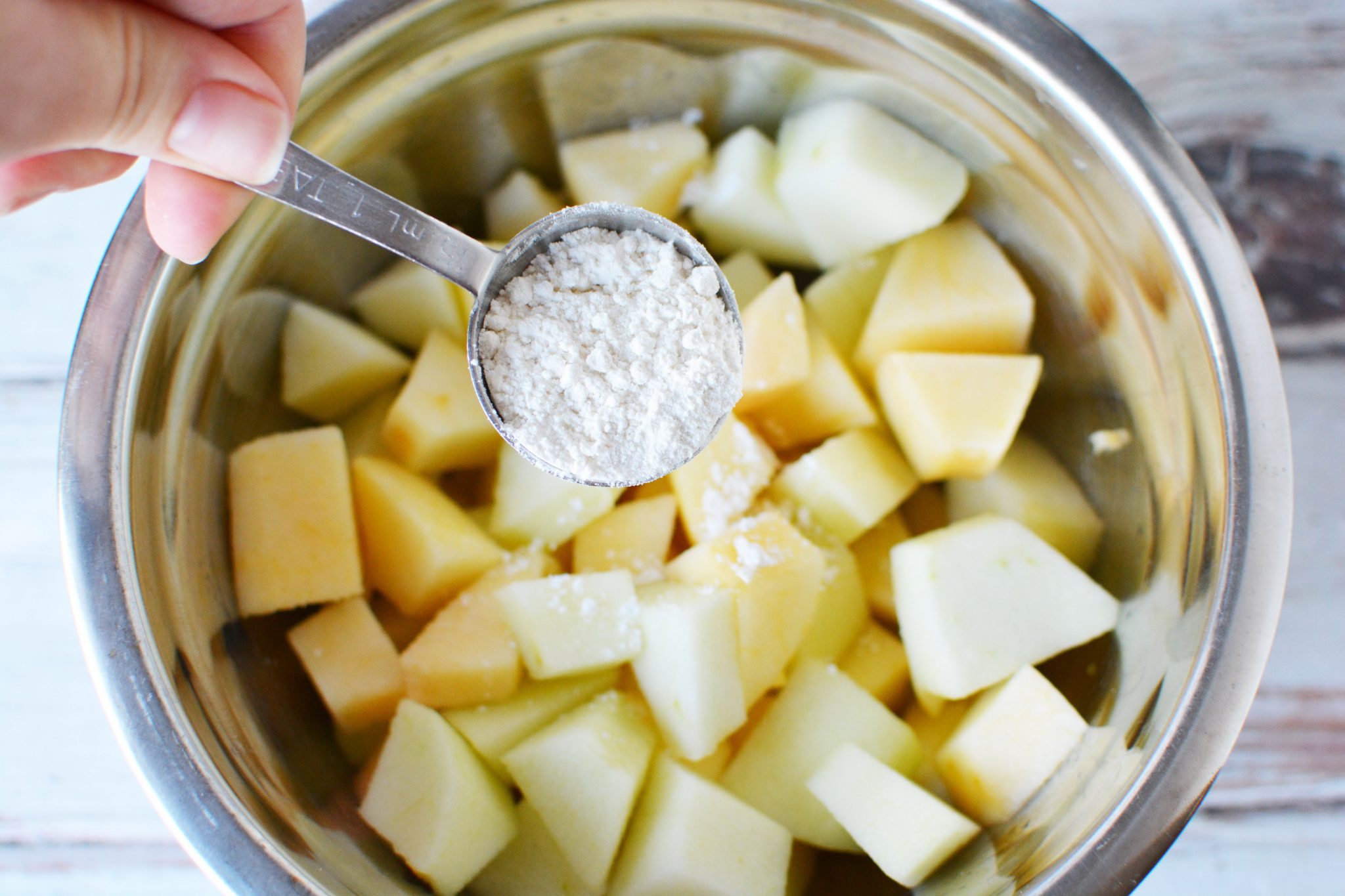 chunks of apples in a bowl with a spoon of flour