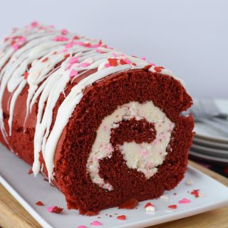 Overhead shot of a red velvet cake roll with white frosting and red and white sprinkles on a platter