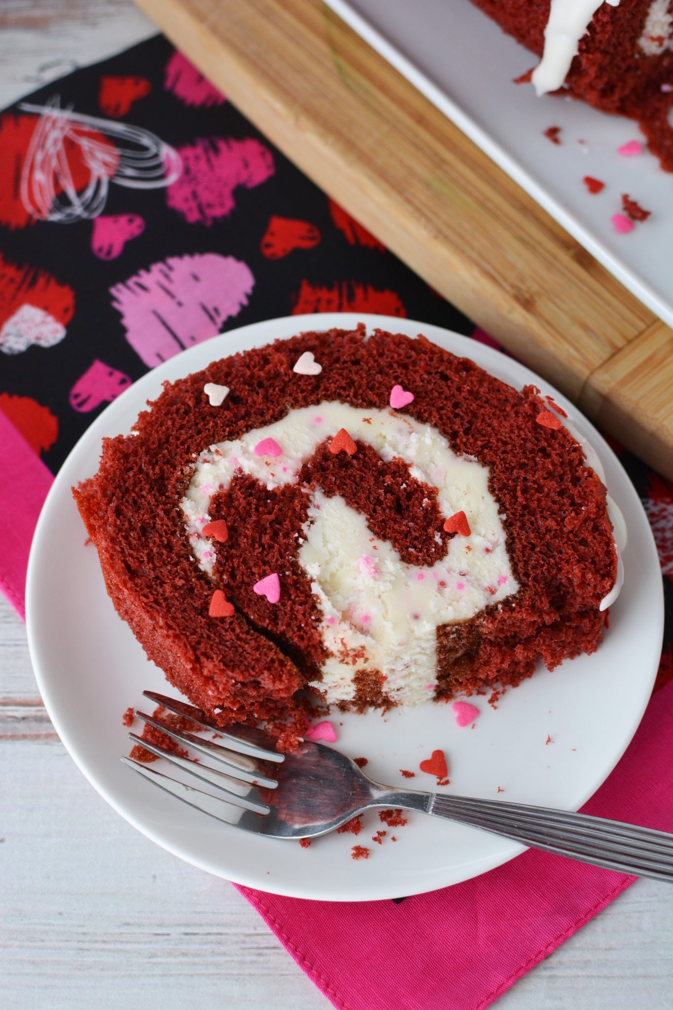 Slice of cake covered in white frosting and Valentine's day sprinkles