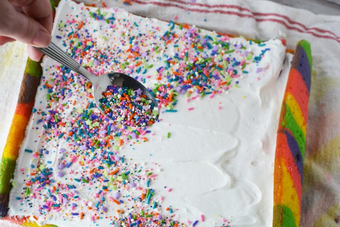 cake roll covered in white frosting and rainbow sprinkles