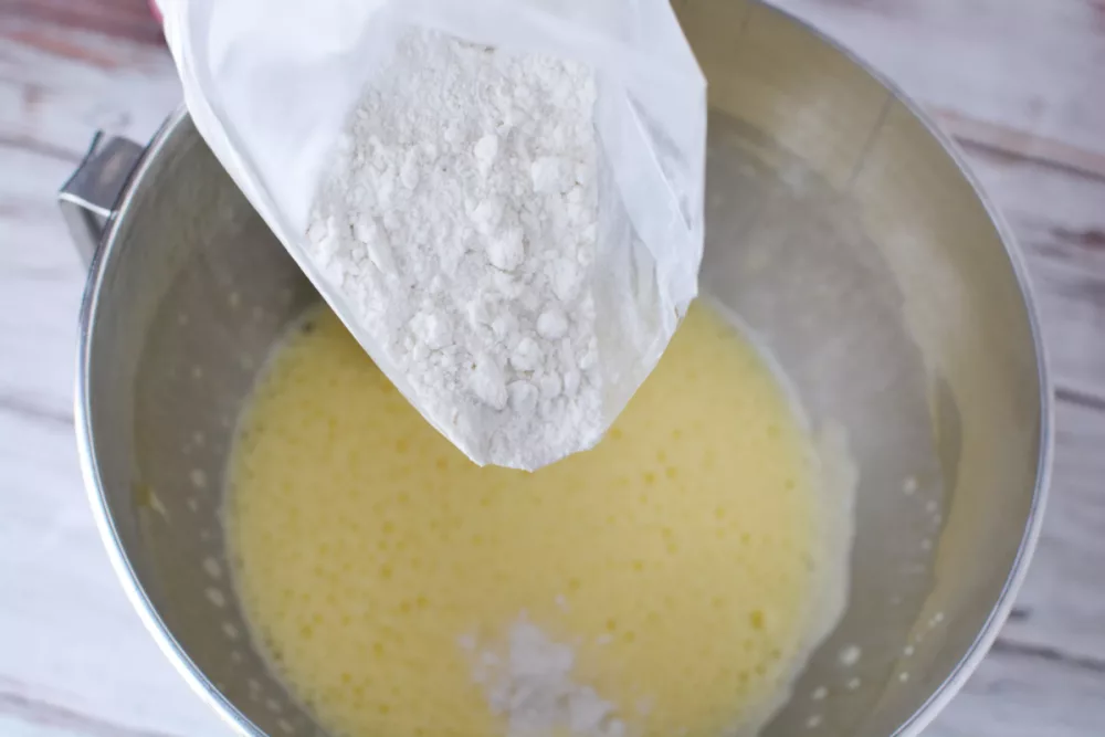 white cake mix being added to a mixing bowl of frothy butter