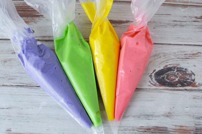 four pastry bags filled with purple, pink, green and yellow cake batter