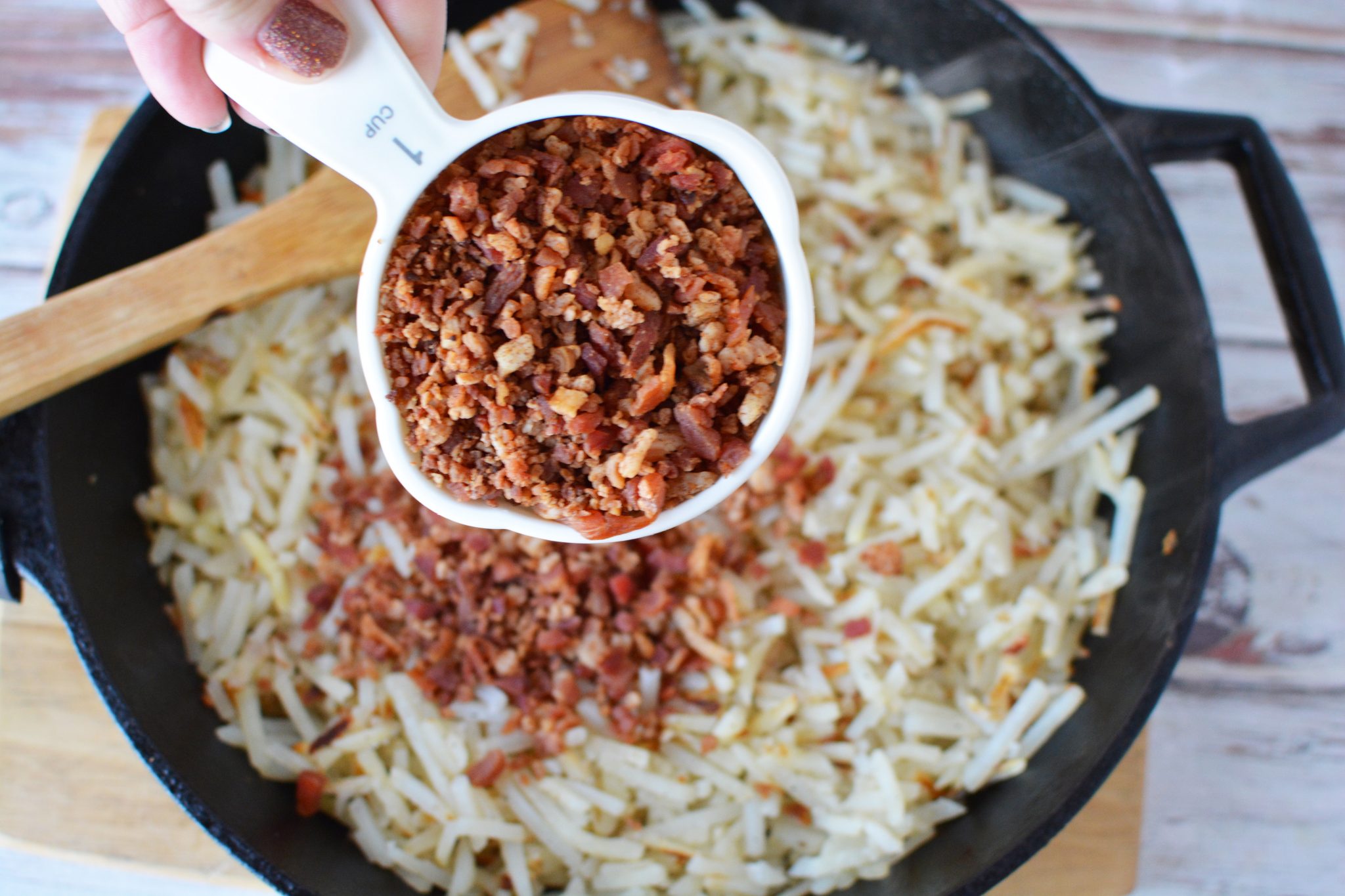 Adding bacon bits to the skillet with the hashbrowns 