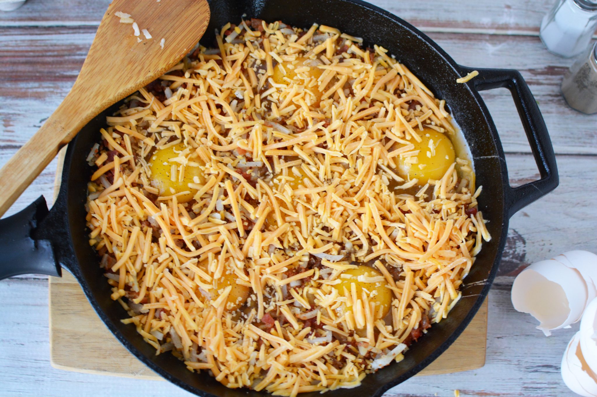 Adding shredded cheese on top of the hashbrowns and eggs 