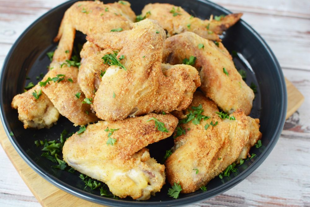 chicken wings covered in a crispy parmesan cheese and sprigs of fresh parsley in an air fryer basket