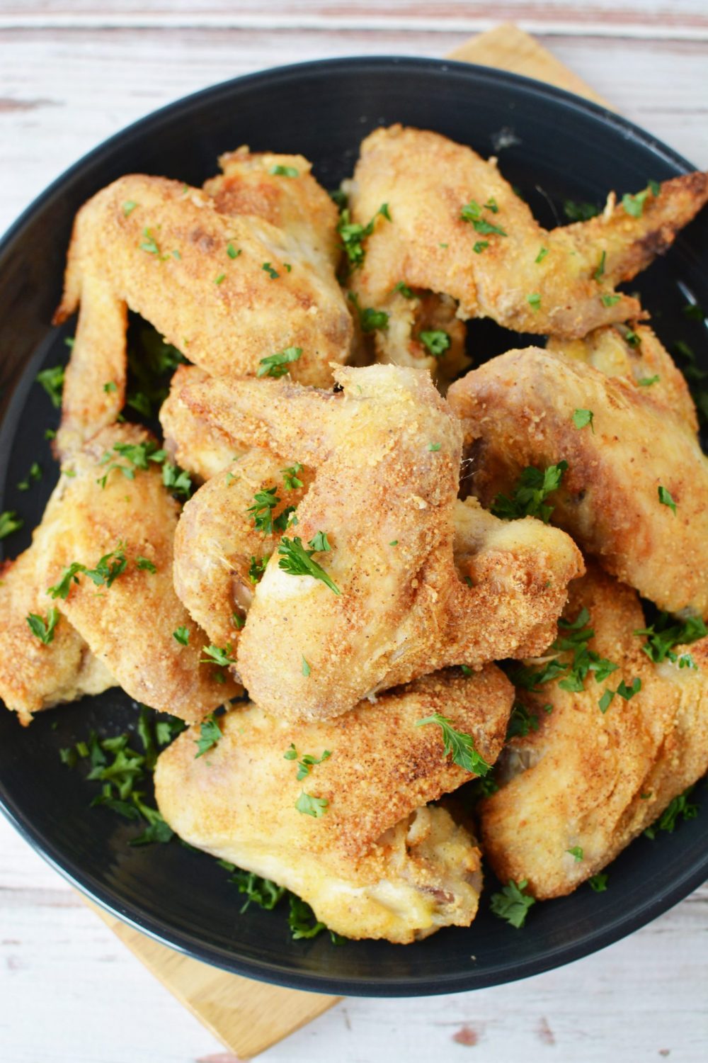 chicken wings covered in a crispy parmesan cheese and sprigs of fresh parsley in an air fryer basket