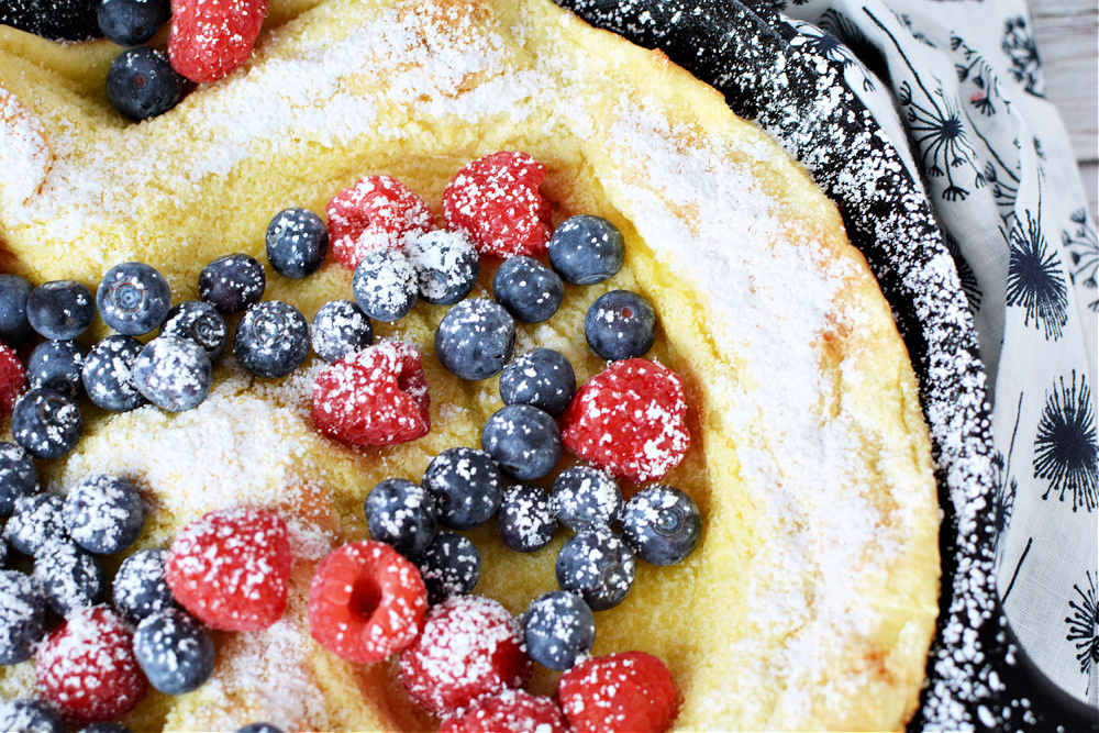 Puffed Pancake in a skillet covered in blueberries, rasbperrise and dusted with powdered sugar