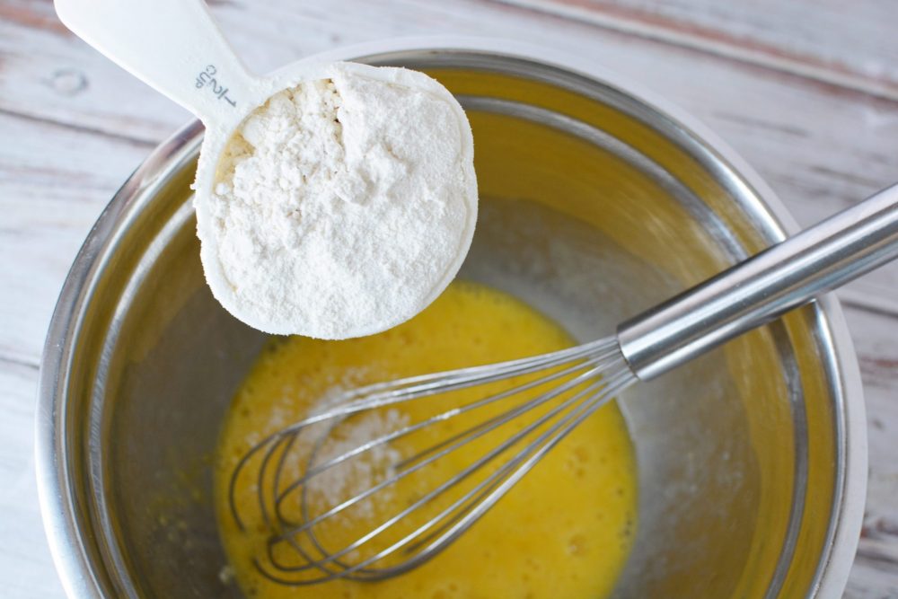 flour being added to an egg mixture in a mixing bowl to make puffed pancake