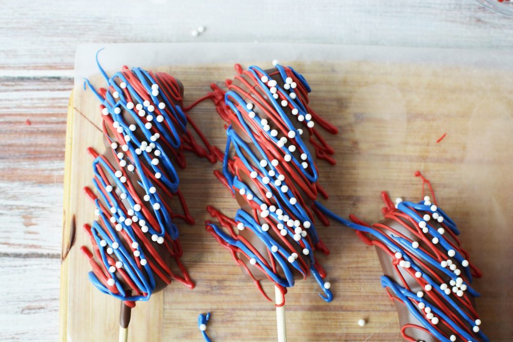 Three Red, White & Blue Marshmallow Pops drying on a cutting board