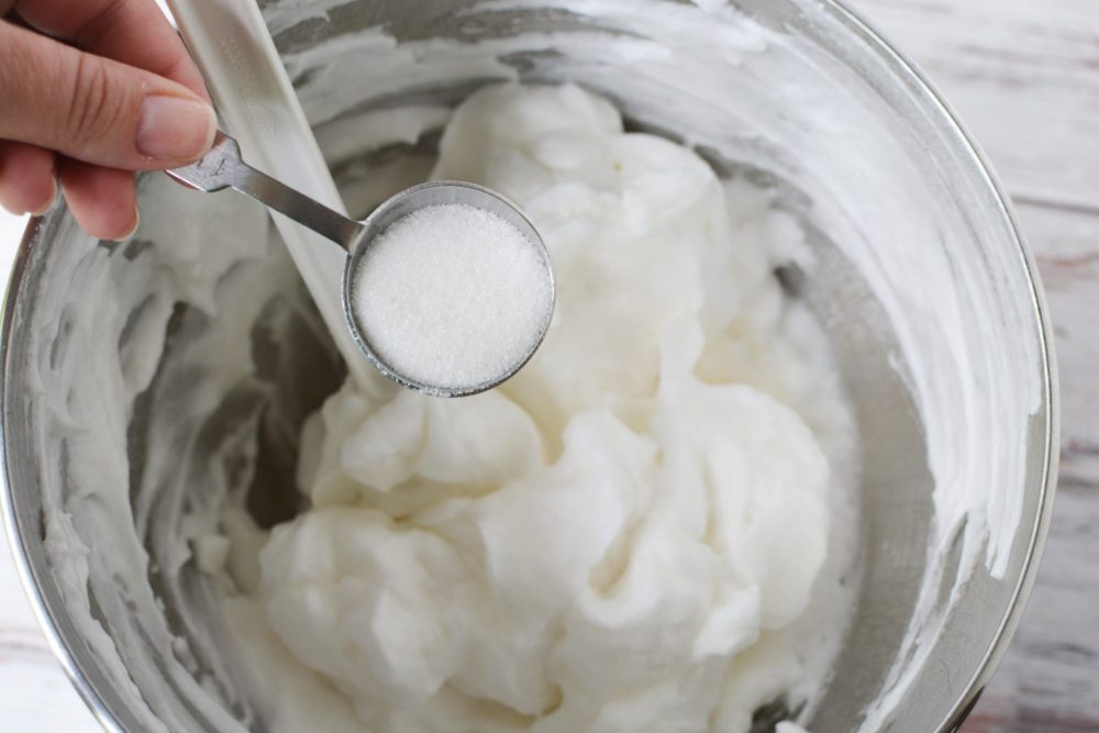 Adding sugar to a bowl of whipped egg whites