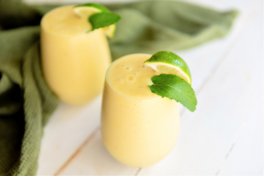 light orange Smoothie in a glass with garnish of lime wedges and mint leafs