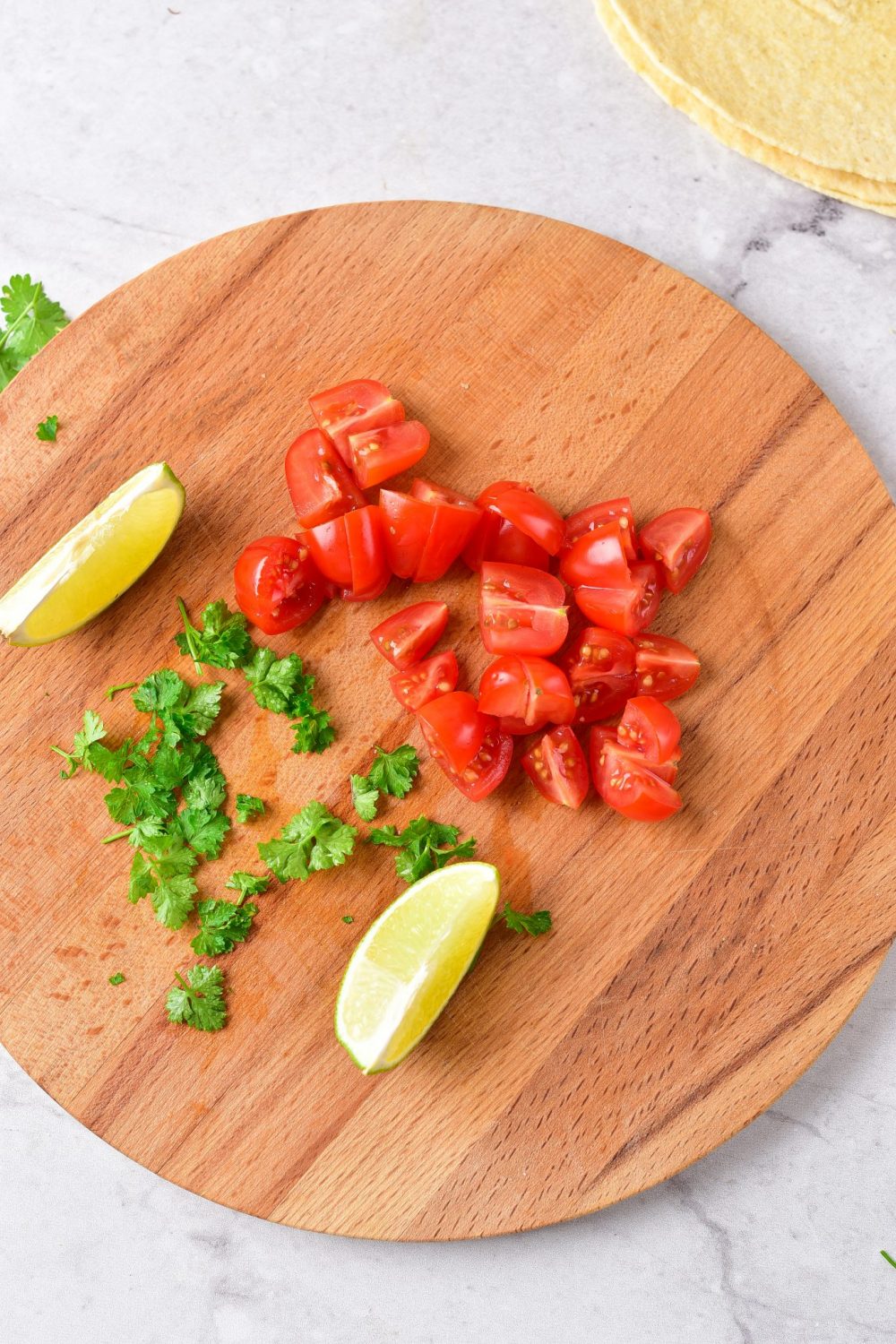 A cutting board with chopped cilantro, tomatoes and lime slices 