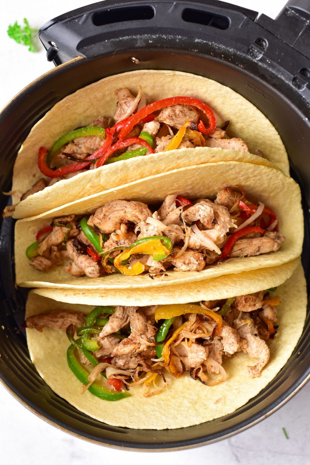 Three corn tortillas in the air fryer basket filled with the chicken and peppers mixture 