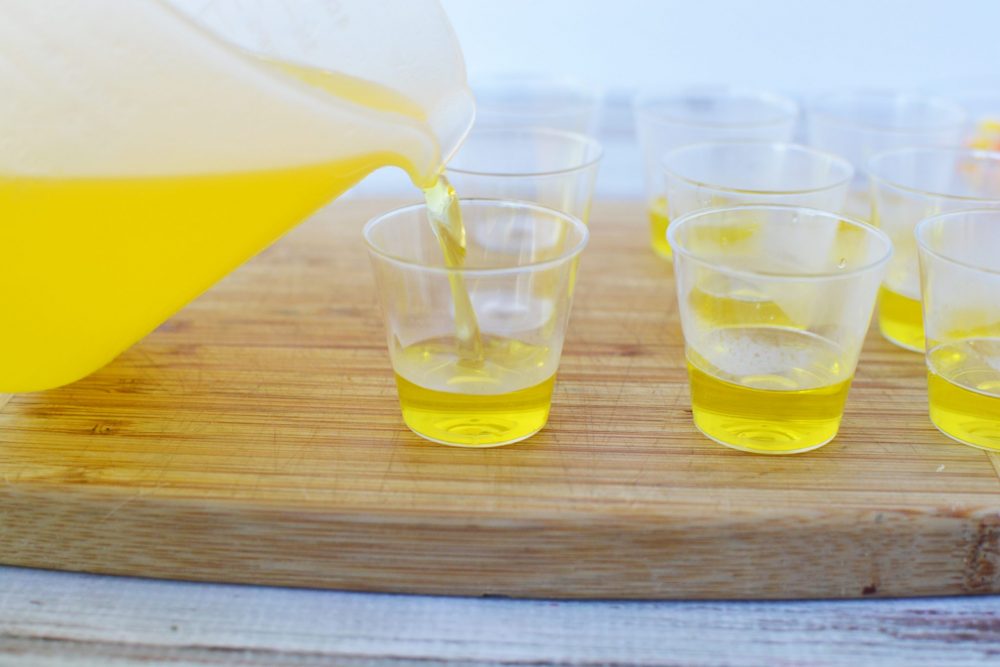 Pouring pineapple gelatin into one-ounce shot glasses 