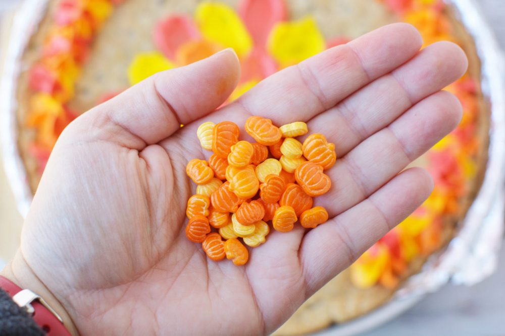 A hand holding sprinkles that are shaped like pumpkins