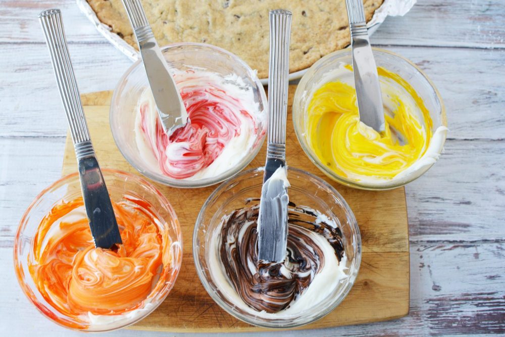 Four bowls of frosting colored red, yellow, orange, and brown