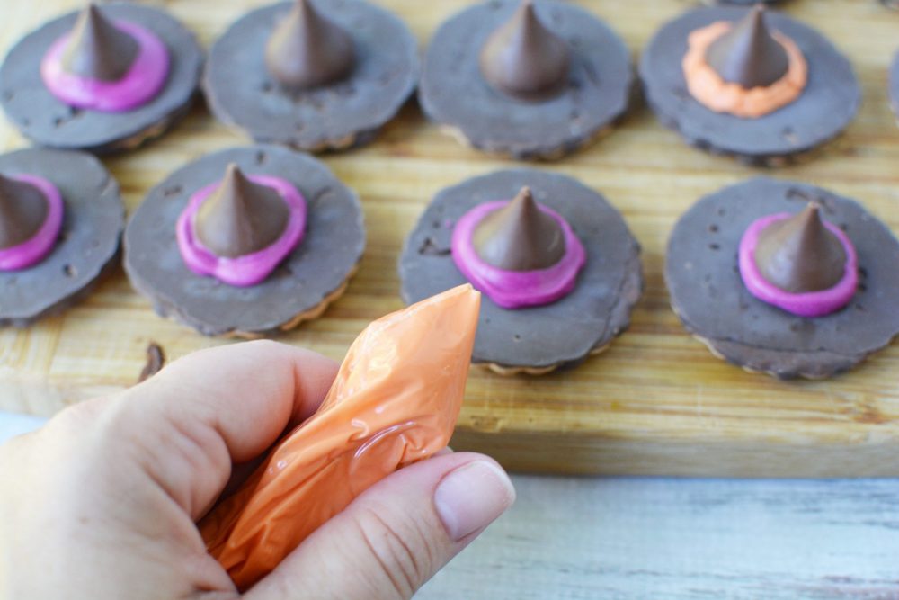 Piping orange and purpose melted chocolate on the Witch's Hat Cookies 