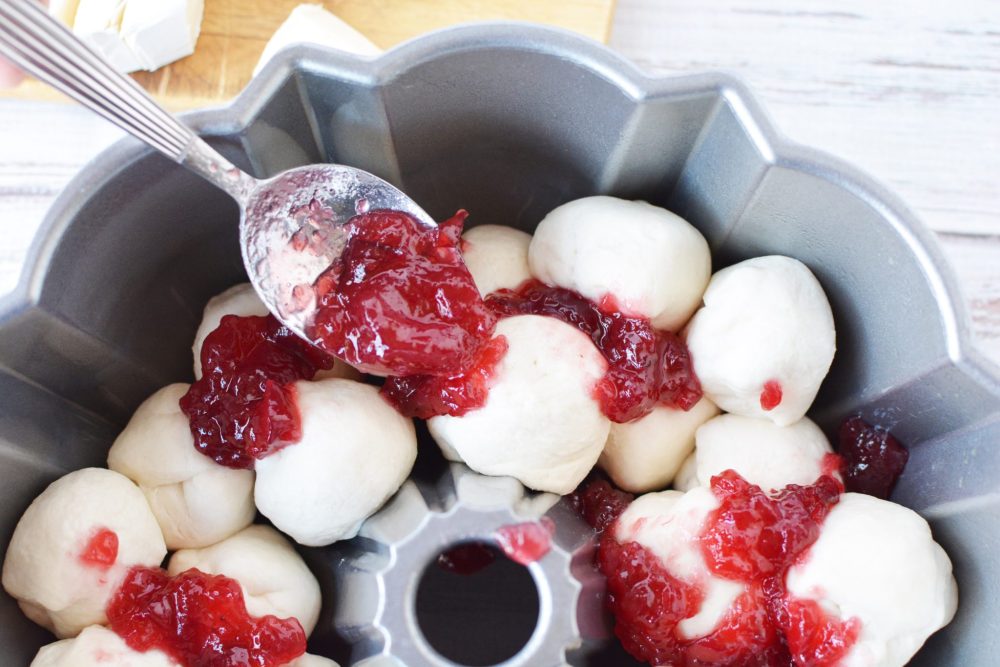 Brie-filled biscuit balls piled in a bundt pan with cranberry sauce on top 