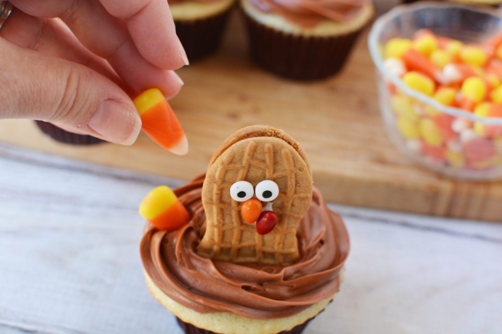 Placing candy corn on a cupcake to look like turkey feathers 