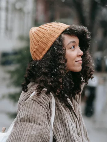 woman with curly hair in a jacket and knit cap in the winter