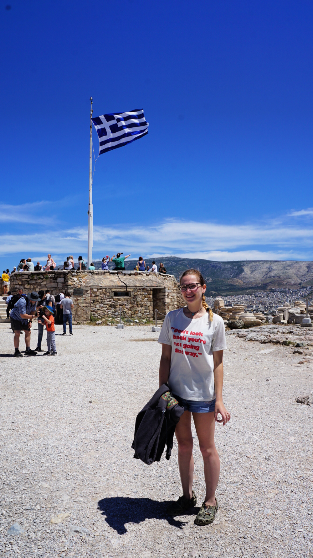 Angeline Pridemore standing in front of the Greek flag at the Acropolis in Athens Greece