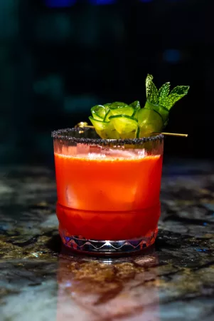 red cocktail in a rocks glass with cucumber garnish