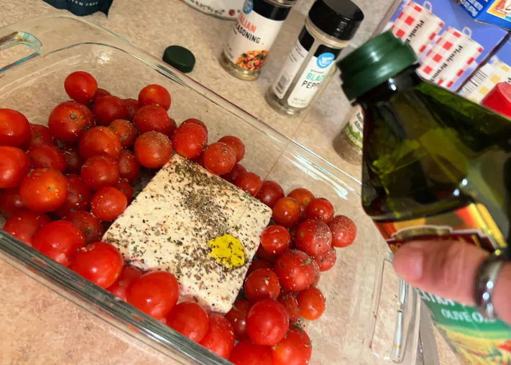 drizzling olive oil over a baking dish of feta cheese and cherry tomatoes