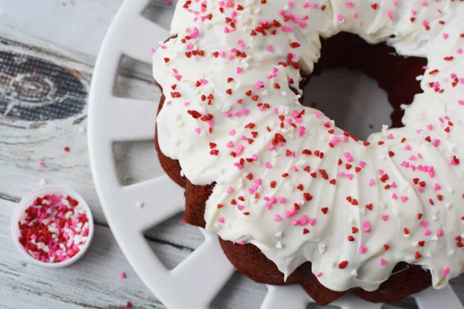 Red Velvet Cake covered in white frosting and valentines day sprinkles