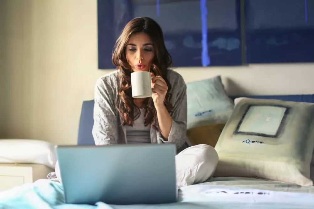 Small Business employee working on a laptop in bed drinking coffee