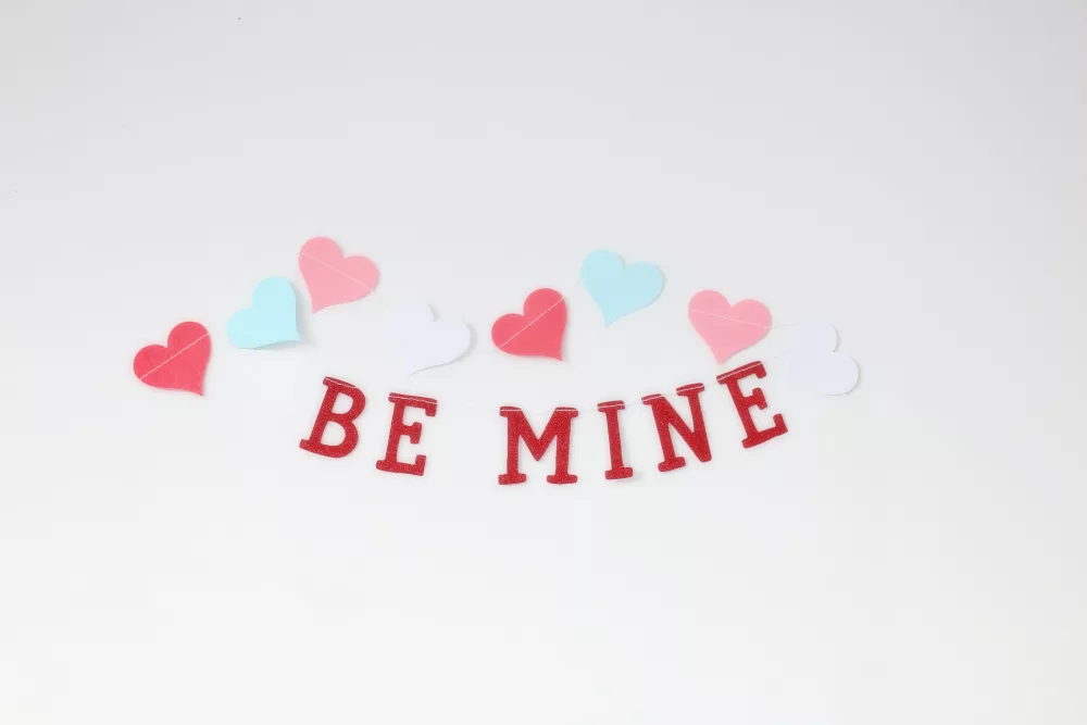 pretty valentine banner reading be mine in red with pink, blue and red hearts on top