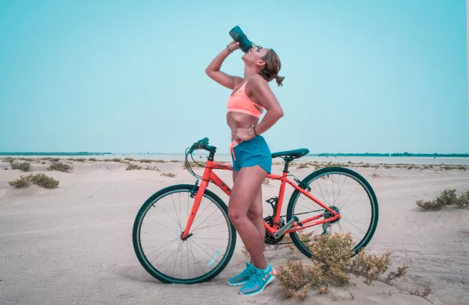 Woman drinking water on a 3 speed bike on the beach