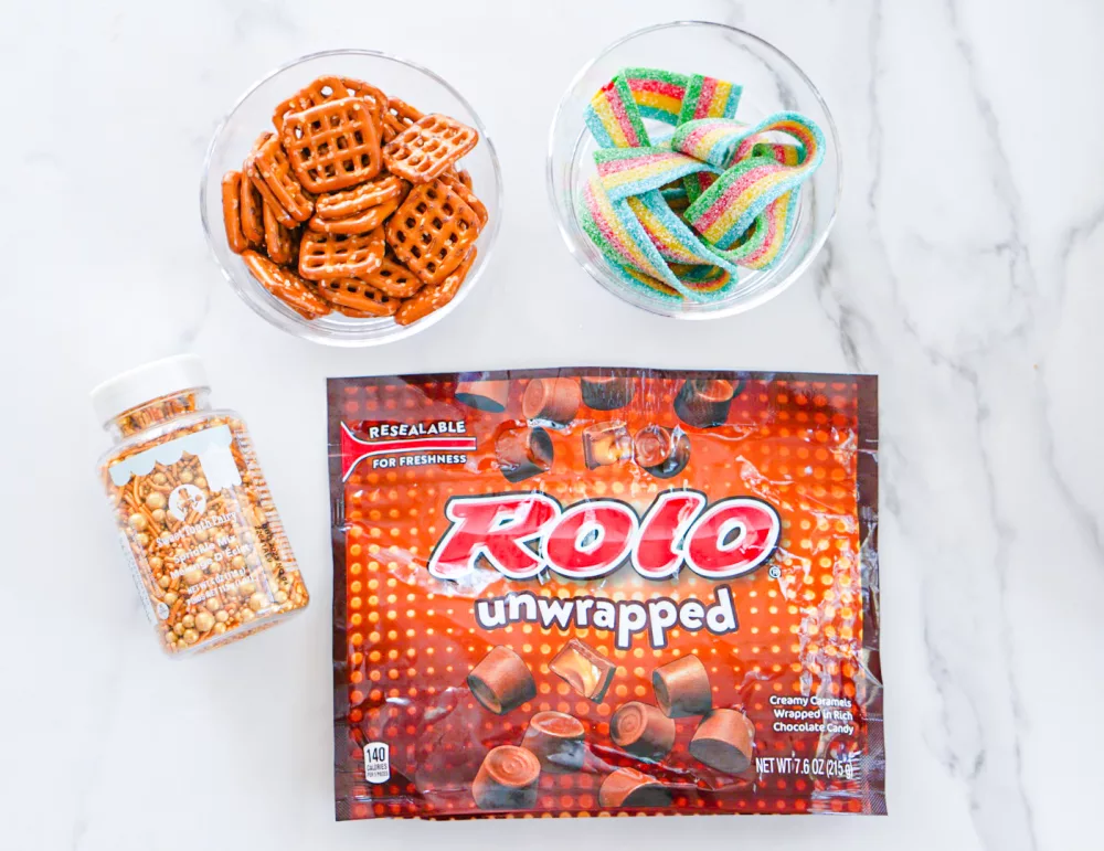Rolo Pretzel Delights ingredients: gold candy sprinkles, pretzels, rolos, and rainbow belt candy
