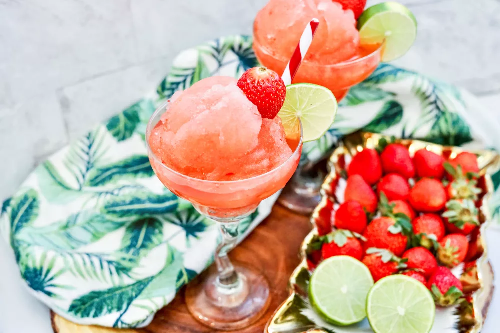 Frozen Berry Margaritas in margarita glasses with fresh strawberries and limes in the background