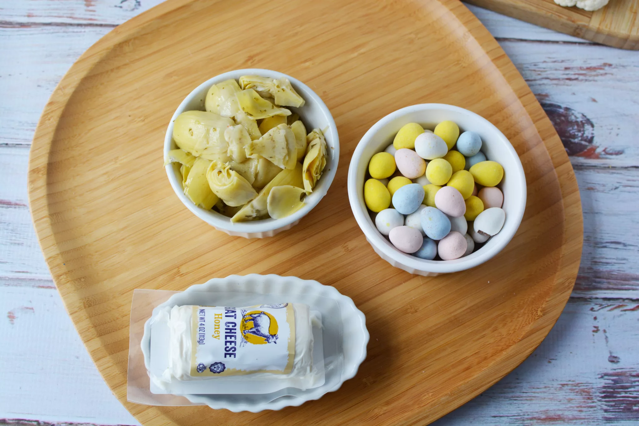 small bowls filled with candy eggs marinated artichoke hearts and honey goat cheese