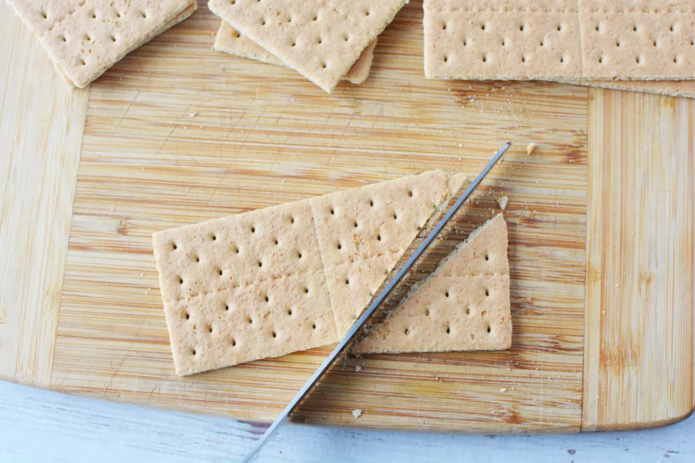 graham crackers being cut to make a gingerbread house