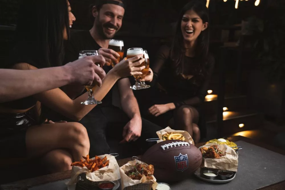 group of people toasting with beer around a table watching the Super Bowl