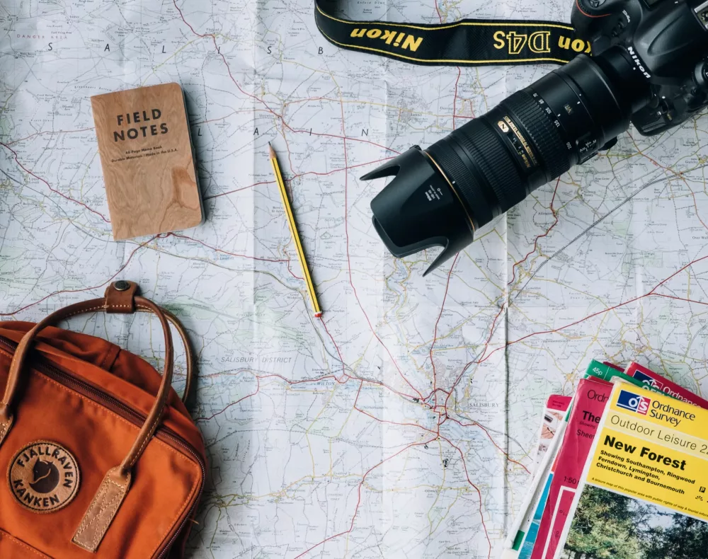 travel items laid out on a map including a camera, map, pen, notebook and bag