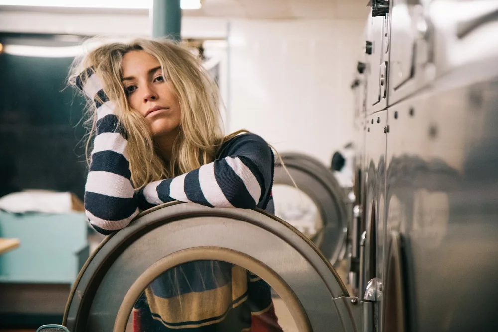 woman standing in front of a commercial washing machine with an exasperated look on her face