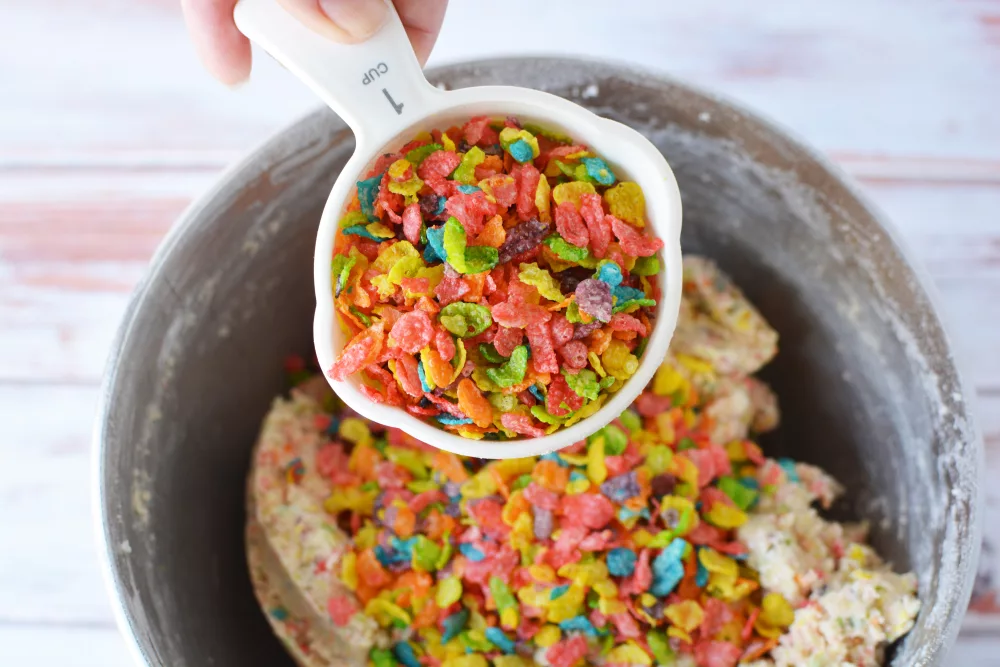 Fruity Pebbles cereal being added to cookie dough