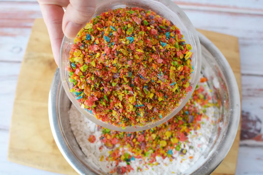 fruity pebbles cereal being poured into a bowl of all purpose flour and other ingredients