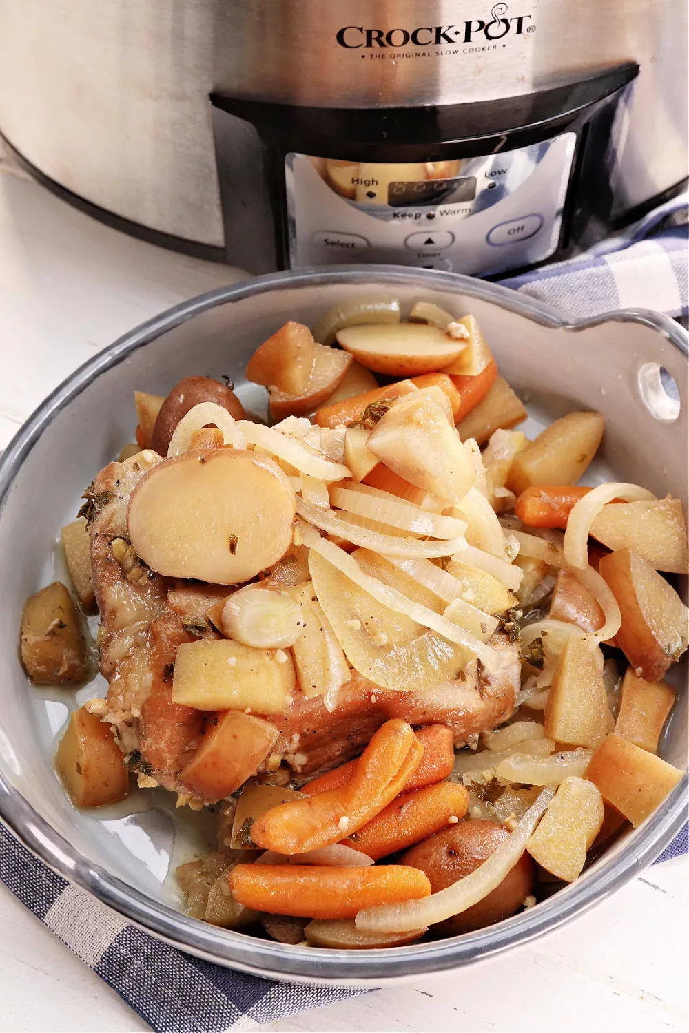 roasted pork on a dish with apples, potatoes, carrots and onions in front of an instant pot
