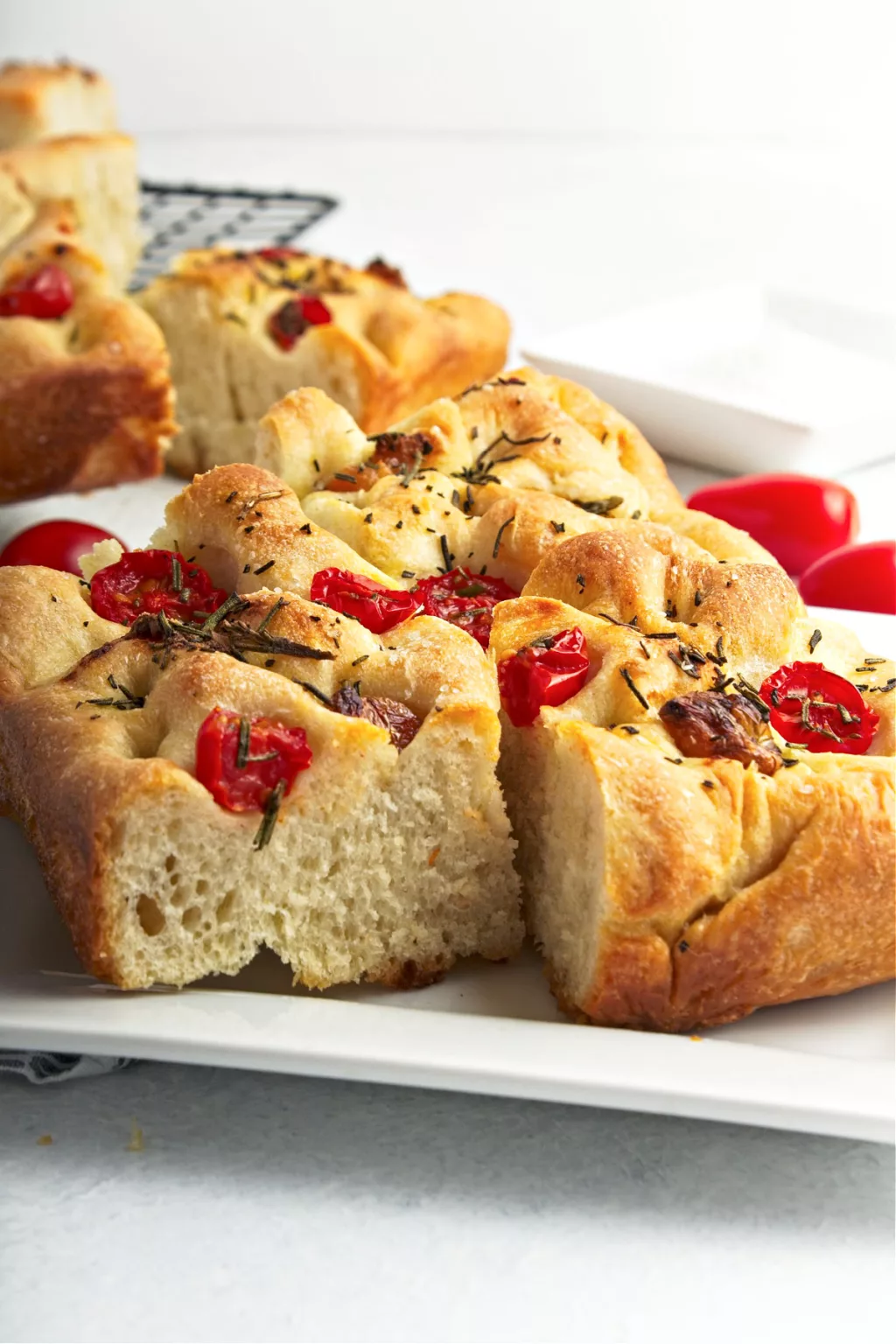 Focaccia bread topped with roasted garlic, roasted tomatoes and rosemary on a black cooling rack