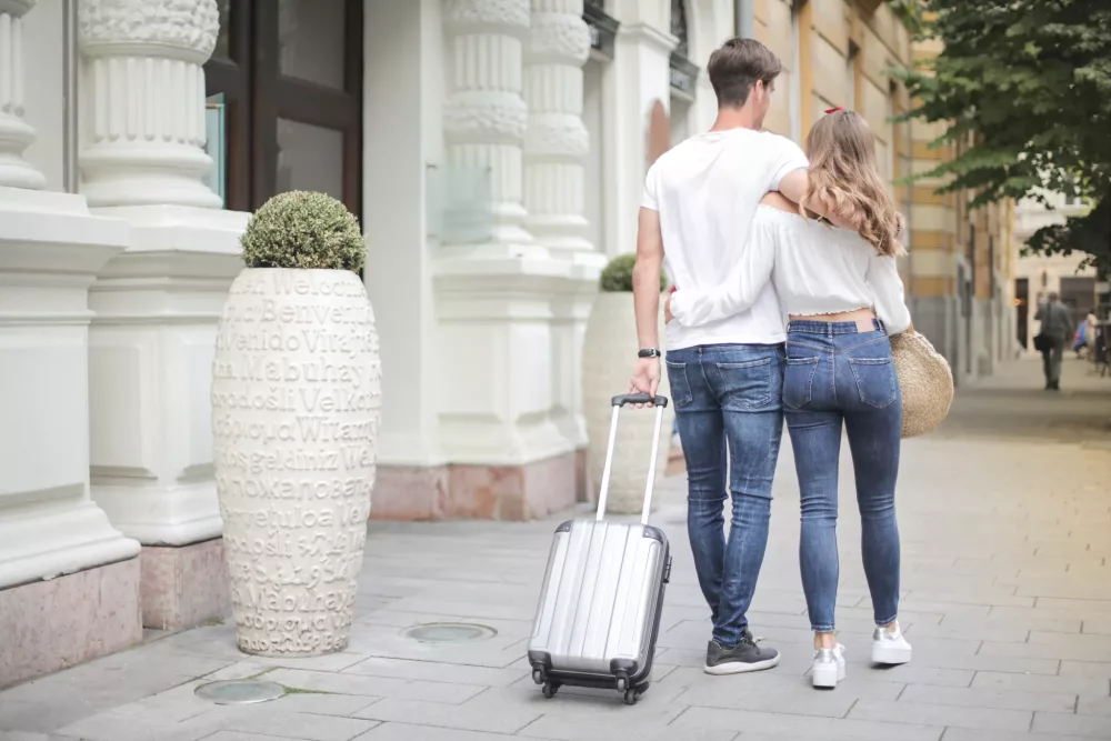 couple walking on sidewalk with their carryon suitcase