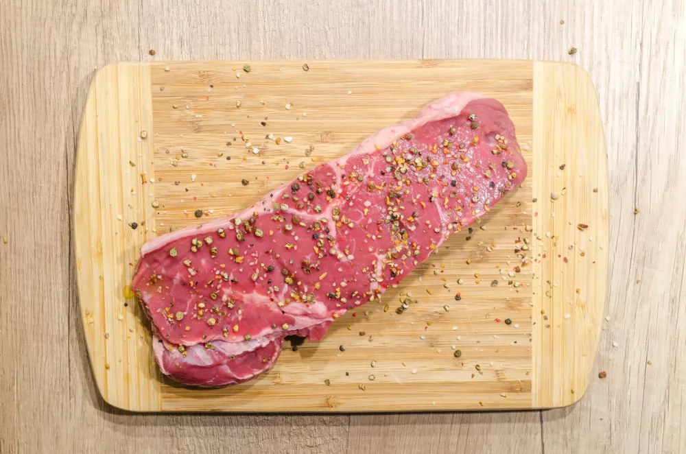 steak covered in seasoning on a wooden cutting board