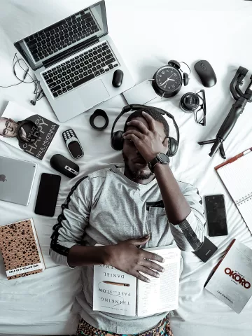 Frustrated man surrounded by technology and electronic devices on a bed
