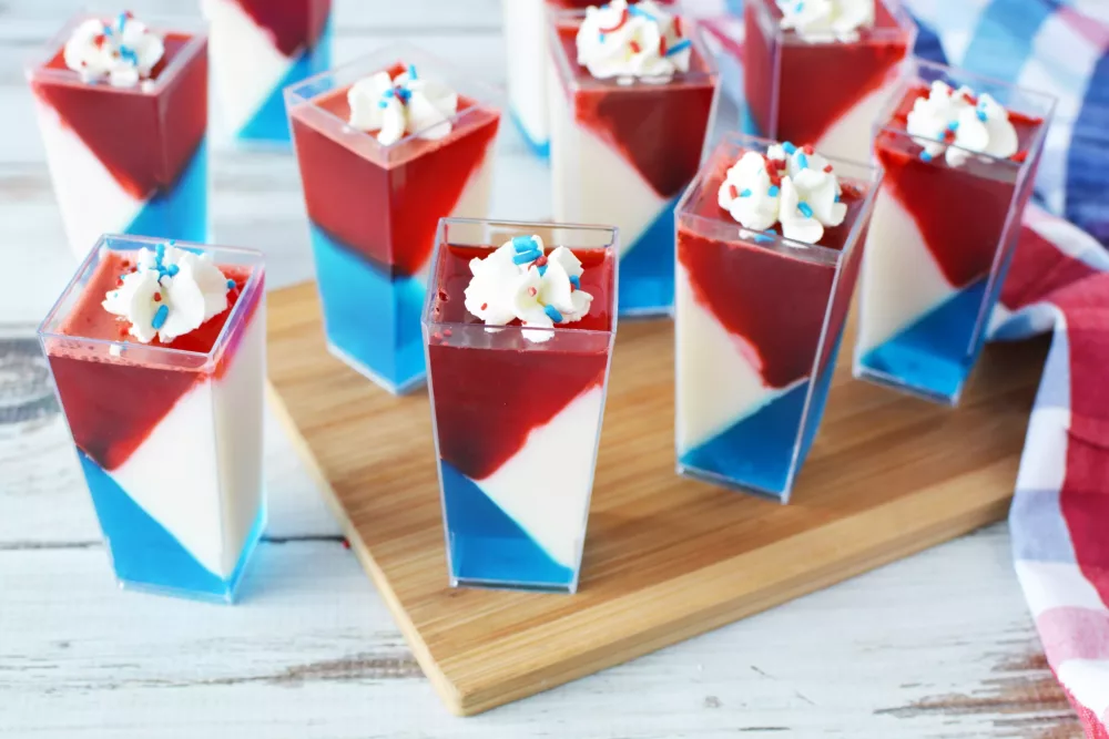 Red White and Blue JELLO Shots in mini cups with whipped cream and sprinkles on top