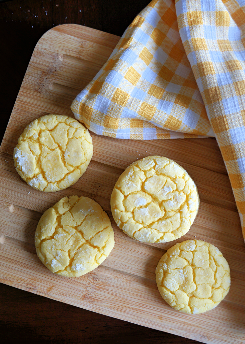 lemon ookies with powdered sugar on top on a wooden cutting board with a yellow and white tea towel